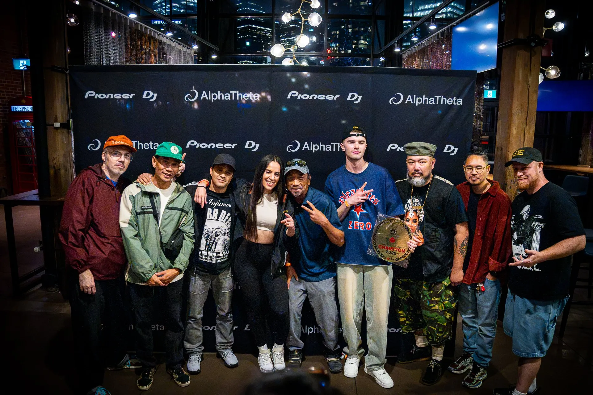 DEEJAY T-JR. with the judges, competitors and the 2026 champion in front of the Pioneer DJ and AlphaTheta sponsor wall.