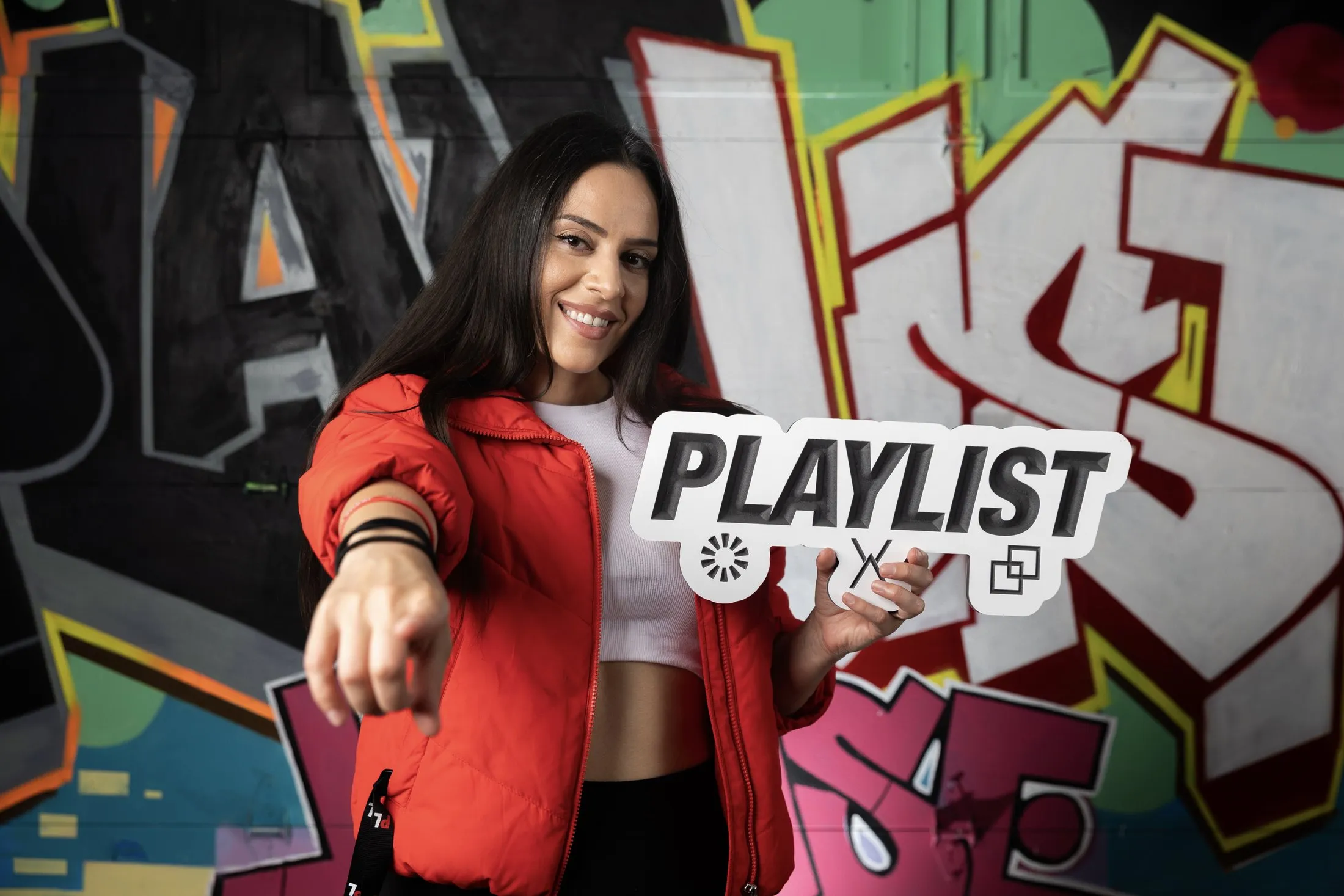 DEEJAY T-JR. holding the PLAYLIST sign in front of a graffiti wall at DJ Jazzy Jeff’s PLAYLIST Retreat.
